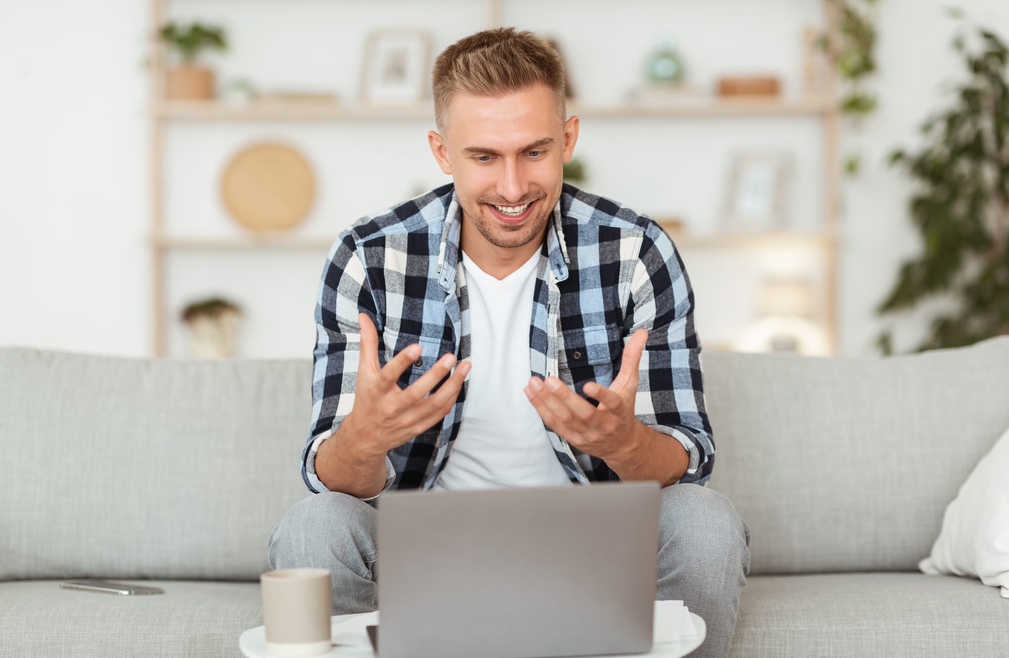 Virtual Conversation. Portrait of young manager having online video call on laptop, talking to webcam. Cheerful man explaining something to client and gesturing, sitting on the sofa at his house